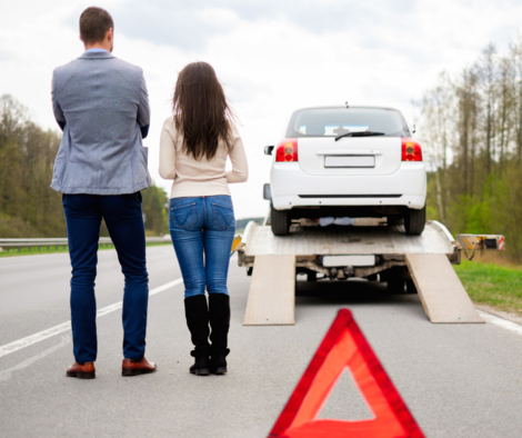 Man and Woman watching their vehicle leave on a tow truck from the side of the road